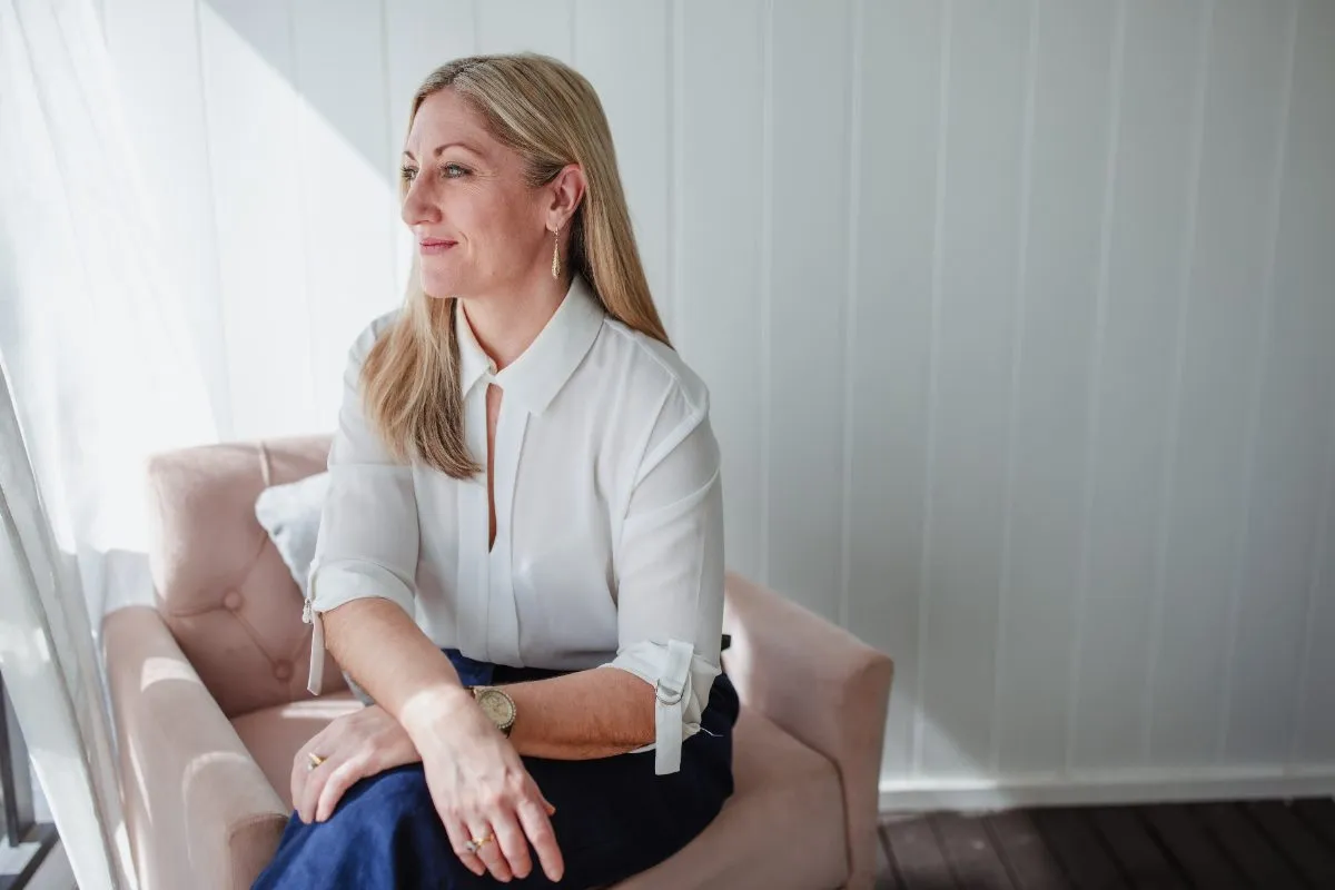 Kristy seated in an armchair by a window, looking out thoughtfully
